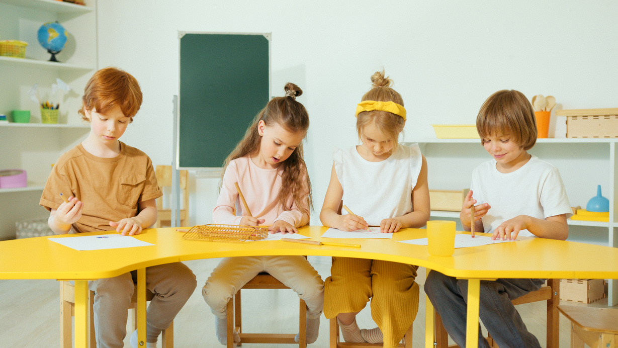 Kids Sitting on Yellow Table Writing 